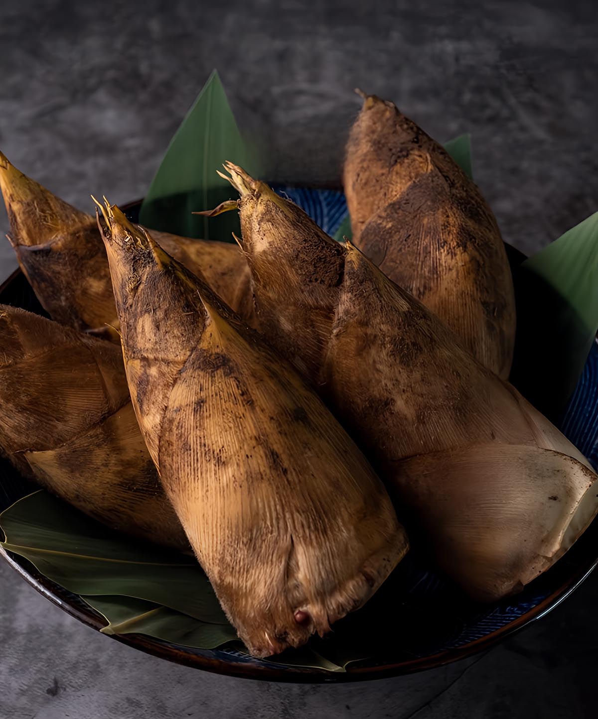Whole bamboo shoots on a plate lined with green leaves