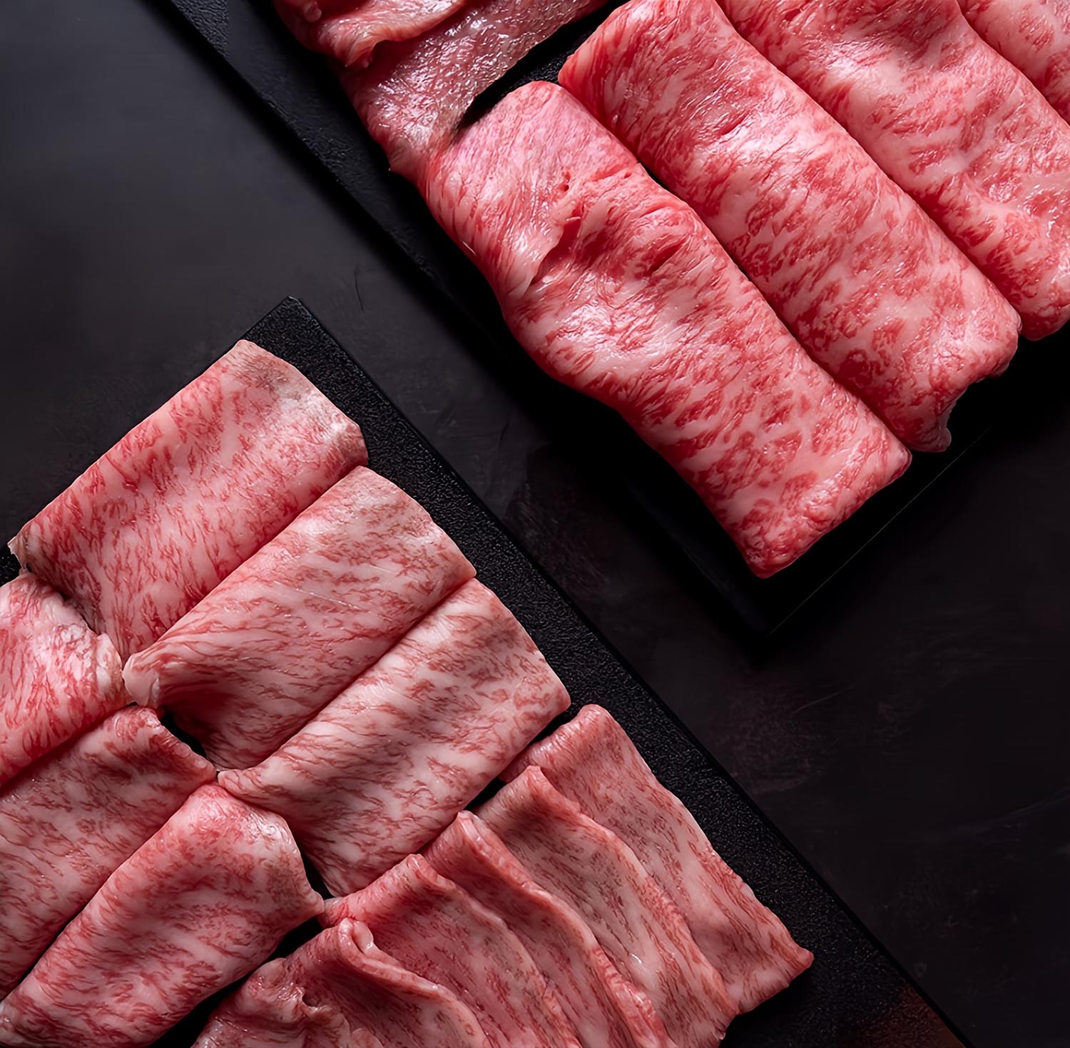 Thinly sliced, heavily marbled Wagyu beef arranged on black trays