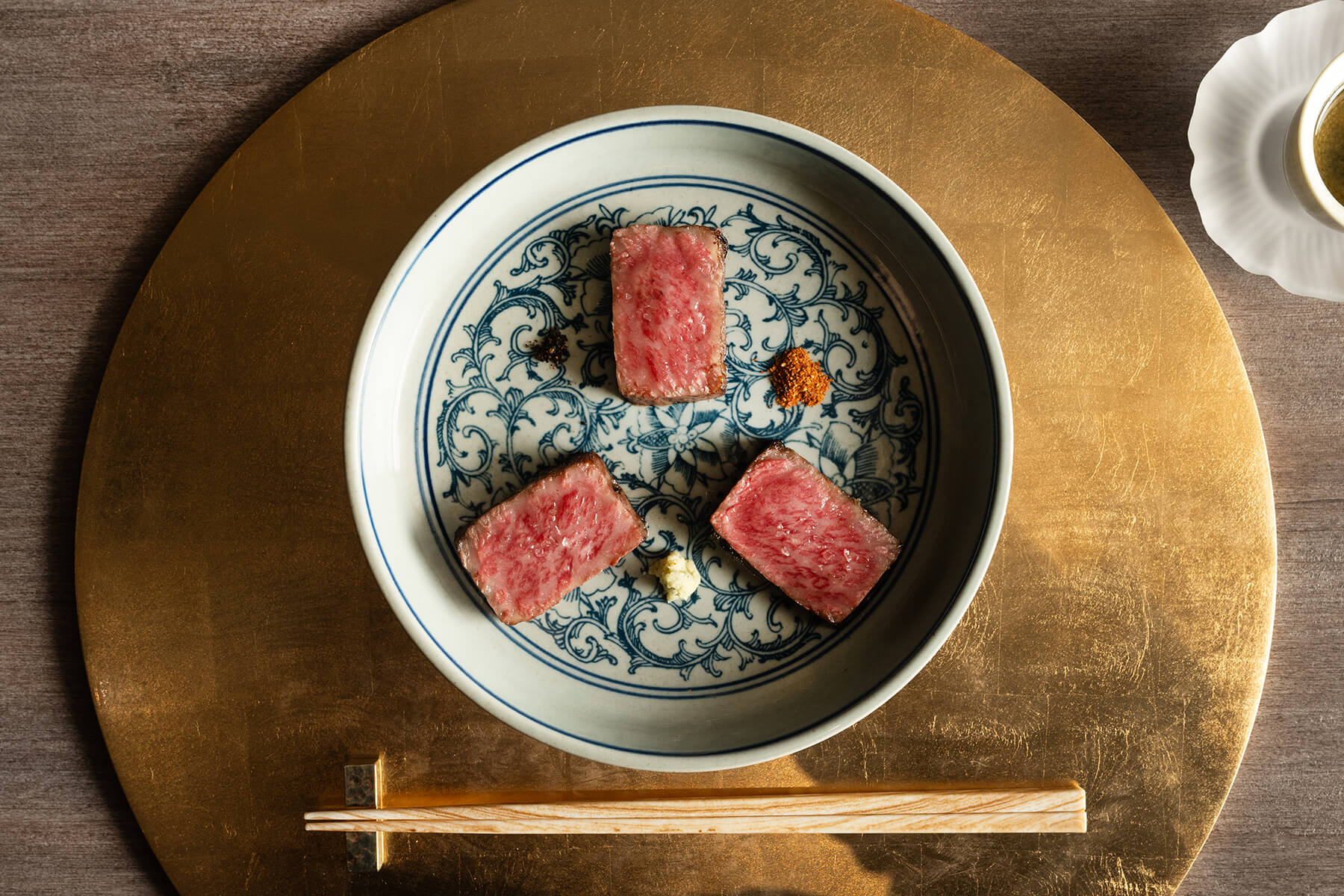 Three pieces of seared Wagyu with seasonings in a patterned bowl